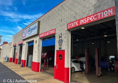 Exterior of C&J Automotive Specialists showing multiple service bays labeled for oil changes, tires, brakes and batteries, and a large “STATE INSPECTION” bay.