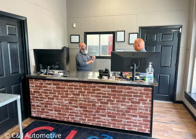 Two C&J Auto staff members talking behind a front counter.
