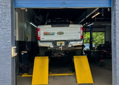 Alignment bay at C&J Auto with a white pickup truck positioned on bright yellow ramps inside the service garage, under a red “ALIGNMENT” sign above the open bay door.