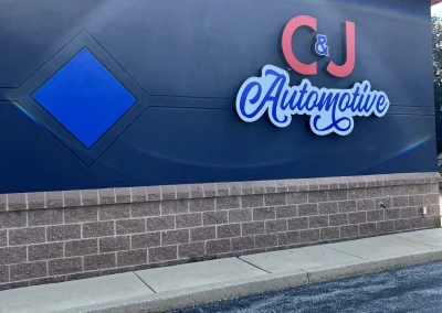 Side view of the C&J Automotive building with the logo sign on a dark blue wall.