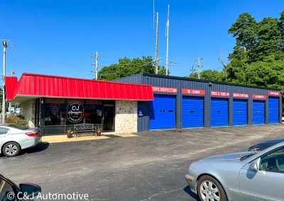Exterior view of C&J Automotive & Tire of Berwyn, an auto repair shop with a red metal roof, stone façade, and multiple blue service bay doors labeled for state inspections, oil changes, tires, brakes, alignment, and suspension services.