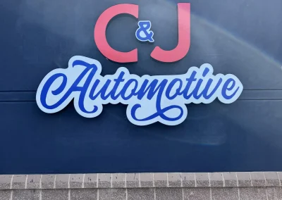 Close-up of the C&J Automotive logo sign mounted on a dark blue exterior wall.