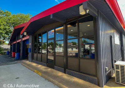 Front entrance of C&J Auto with large glass windows, red-trimmed roof, and open service bays.