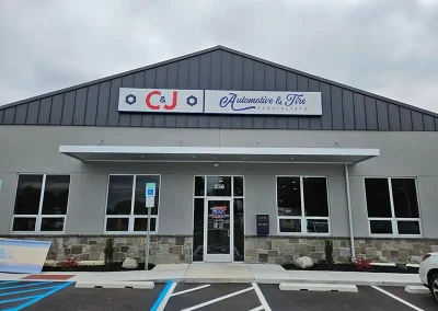 Front view of C&J Automotive & Tire Specialists of Sewell, a gray metal building with a peaked roof, glass entry door with key drop box, and a striped parking lot.