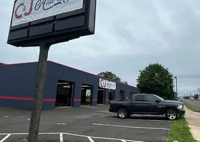 Roadside pole sign for C&J Auto & Tire in Warminster in front of the navy blue shop building with open service bays and a black pickup truck parked in the lot.