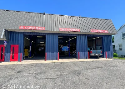 Exterior of the C&J Auto with three open service bays labeled oil change and brakes, tires and alignment, and state inspection, showing vehicles being serviced inside.