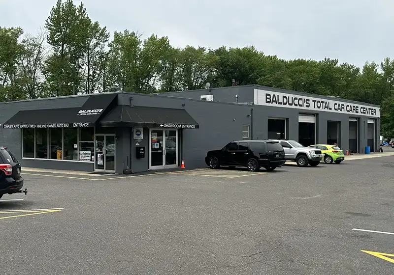 Exterior of C&J Automotive in Cherry Hill featuring a gray auto repair facility with showroom entrances, multiple open service bays, and several customer vehicles parked in front.