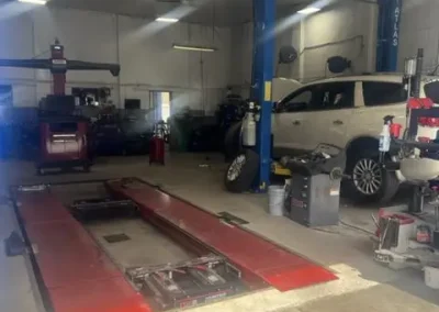Wheel alignment bay at C&J Auto with a white SUV positioned on an alignment lift and diagnostic and tire equipment set up around the shop.